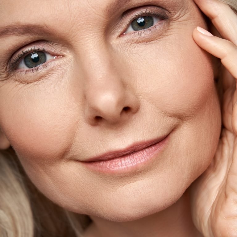 Happy attractive 50 years old middle aged mature woman touching healthy soft face skin looking at camera. Anti age dry skin care tightening treatment ads. Face close up view crop detail portrait