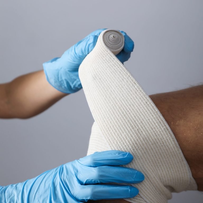 Concept of help during an injury, doctor wrapping knee in bandage on white background